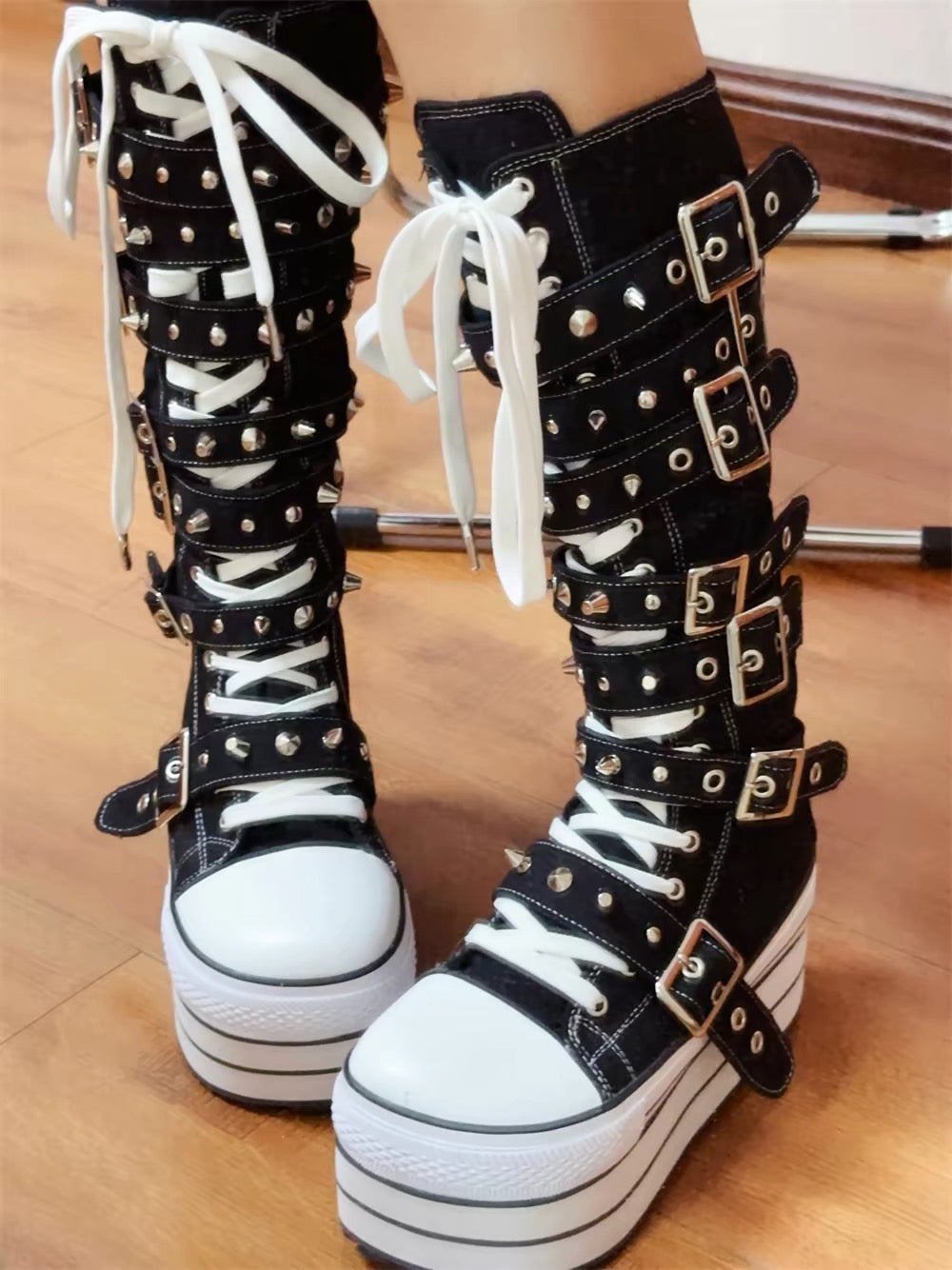 Black and white knee-high platform boots worn with layered buckle straps and white laces