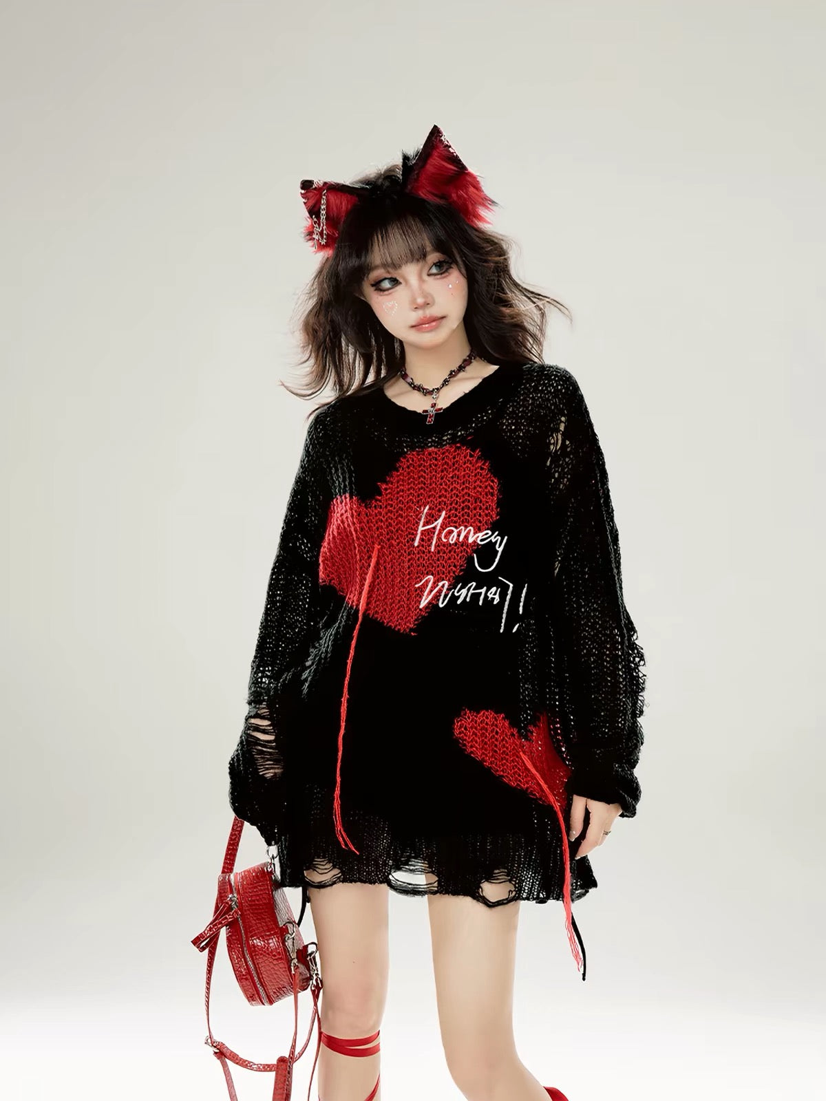 Model wearing black distressed knit sweater with red heart graphics