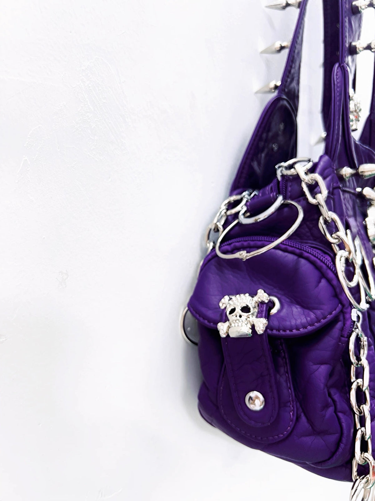 Side detail of purple shoulder bag with skull clasp and silver chain hardware