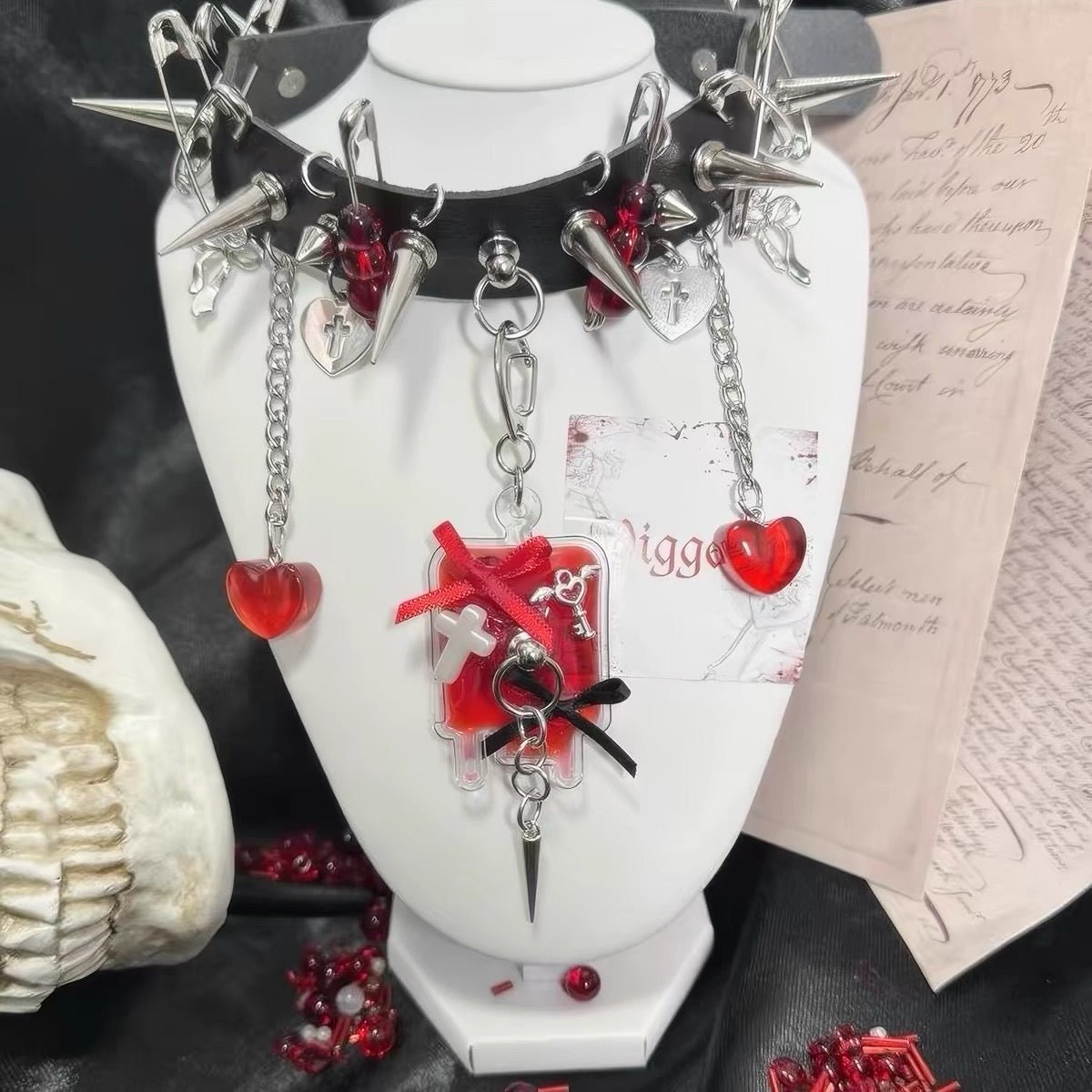 Black choker displayed with red heart charms, spikes, chains and cross details