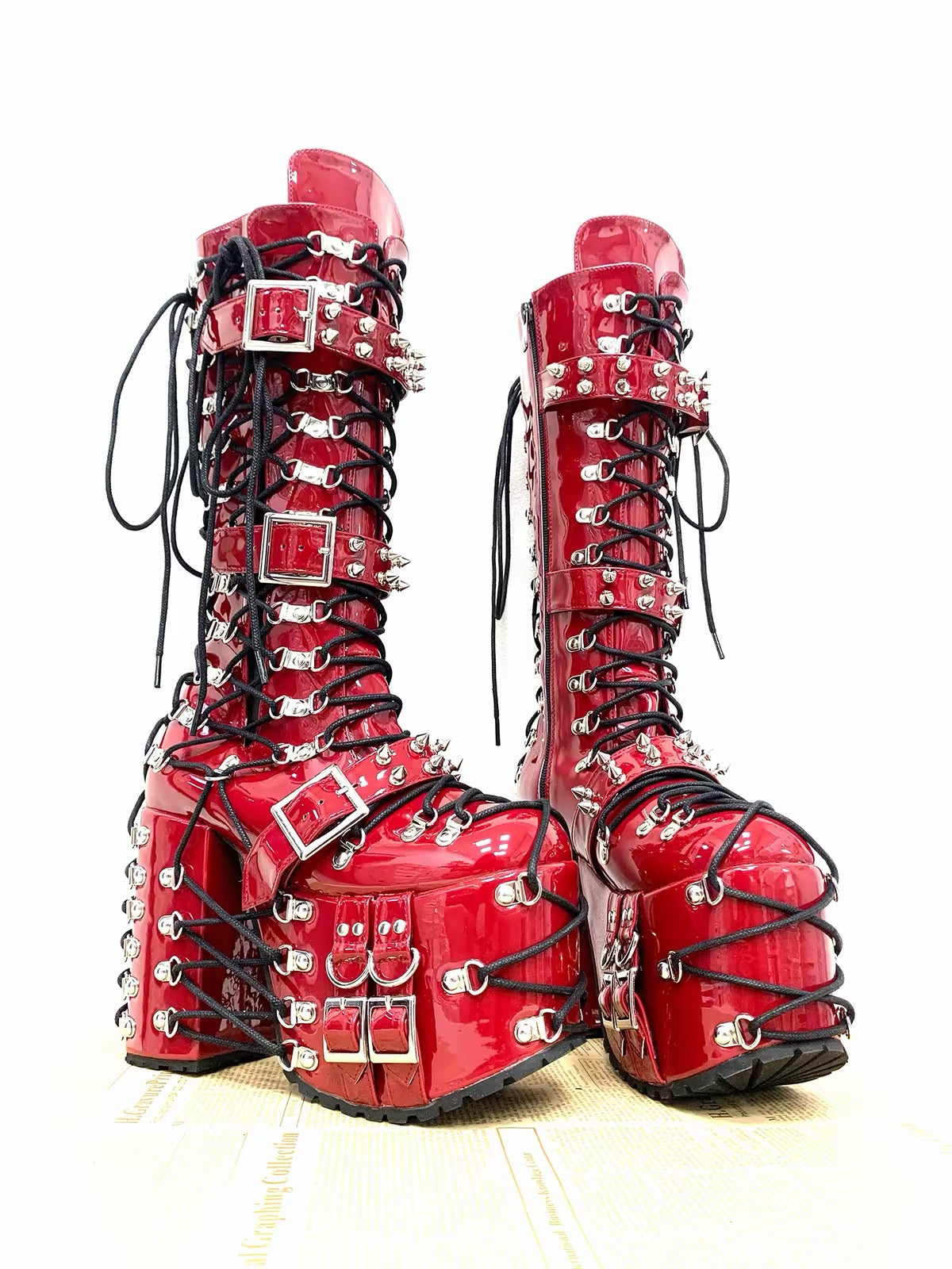 Red patent knee-high platform boots with black laces, buckles and silver spikes